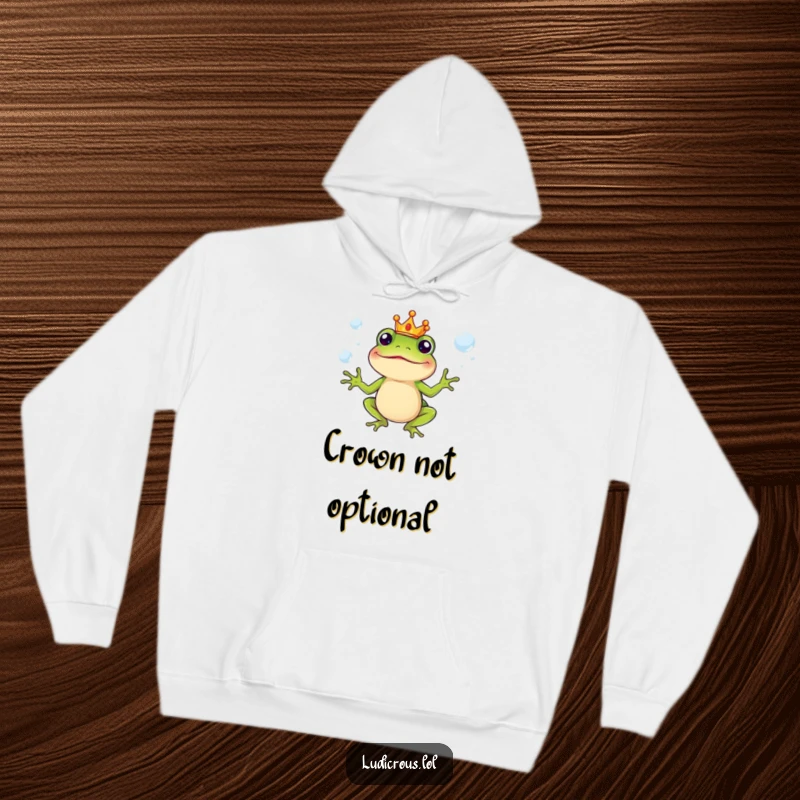 Funny Hoodie showing a silly frog character in a tiny crown, juggling slippery soap bubbles, warm and whimsical.