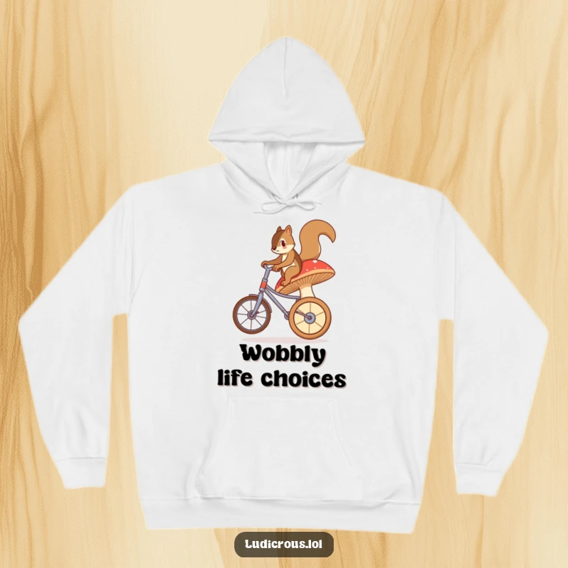 Funny hoodie with a bewildered squirrel struggling to ride a giant, wobbly mushroom like a unicycle, capturing a moment of comical effort.