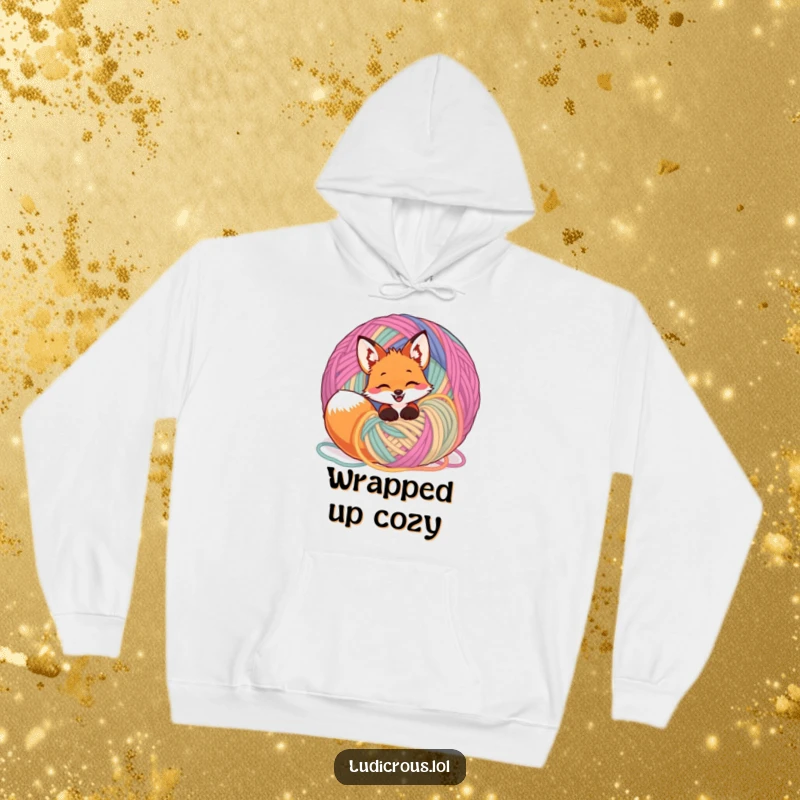 Funny giggling fox wrapped in a huge ball of colorful yarn, embodied on a cozy hoodie for warm and humorous wear.