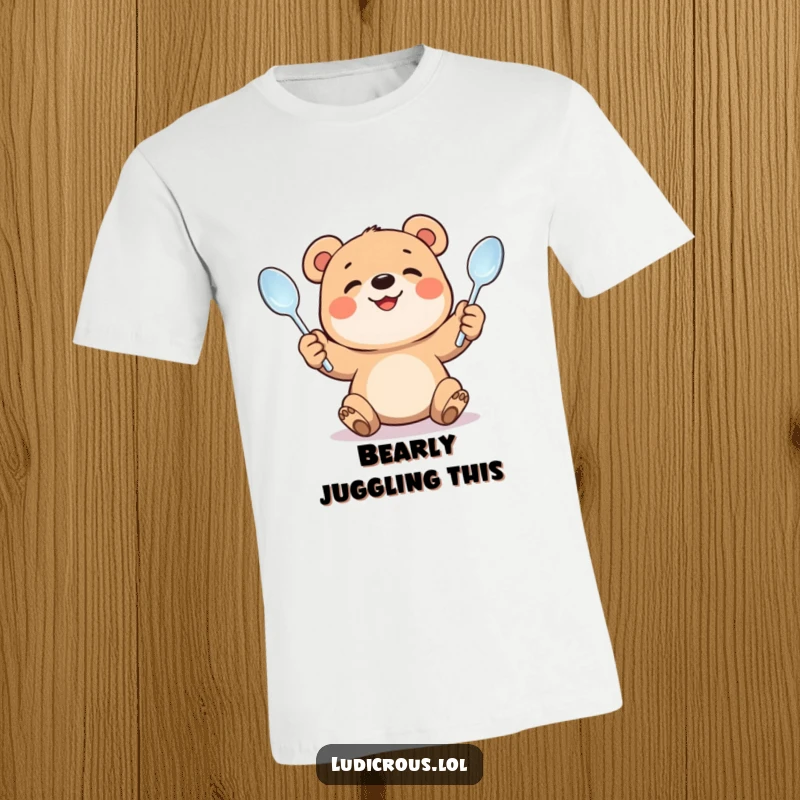 Funny t-shirt print of a smiling bear cub putting great effort into juggling bent spoons. Humorous and adorable depiction of trying hard.