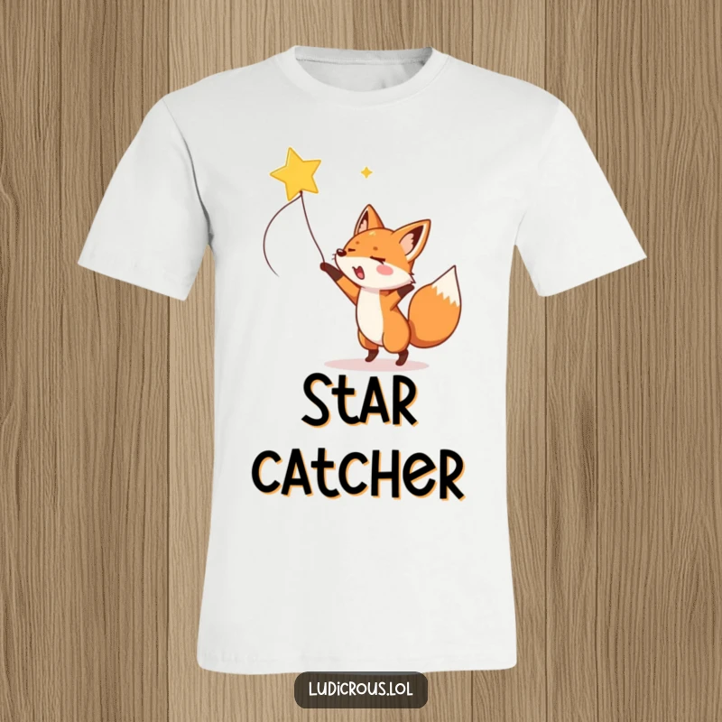 A gleeful fox enthusiastically lassoes a shooting star with a rope on a humorous and adventurous t-shirt.